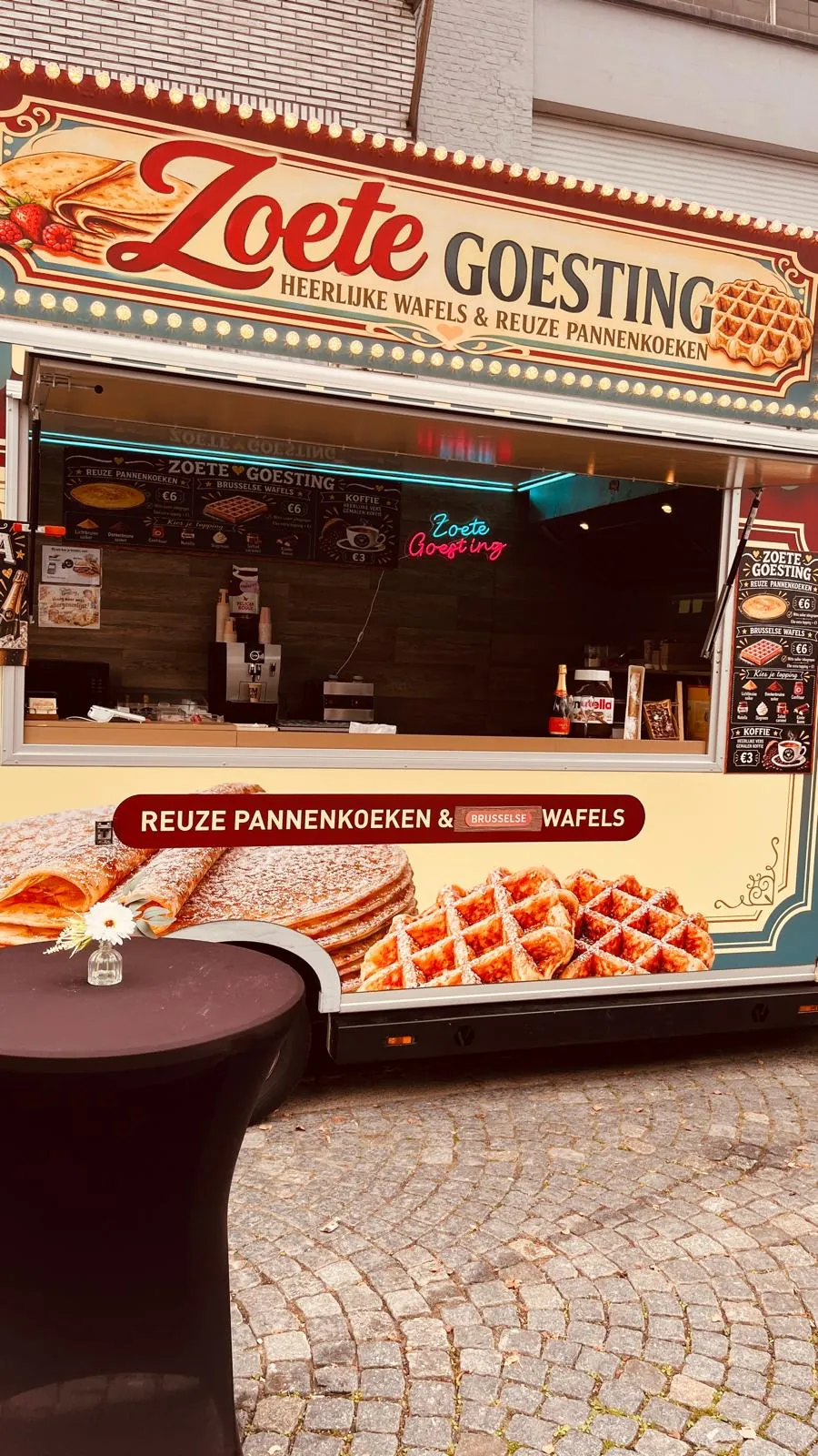 De foodtruck van Zoete Goesting opgesteld op een plein, met een statafel en een bloemetje ervoor